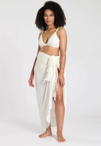 Conjunto de bikini de dos piezas que presenta un bikini texturizado en color crema con detalles dorados y una falda envolvente a juego con flecos y una abertura lateral.