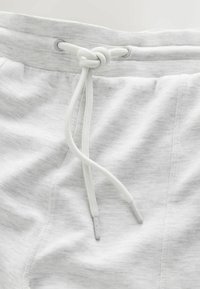 Light gray sweatpants feature a soft, heathered texture, elastic waistband with a white drawstring, and two side pockets.