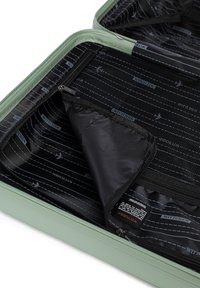 Expandable green suitcase with horizontal ribbed texture, black interior featuring pocket with zipper, and printed airplane designs on fabric.