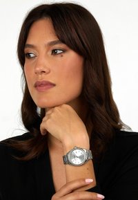 Orologio da polso argento con quadrante rotondo, cinturino in metallo e design minimalista. Presenta una lunetta testurizzata, un quadrante numerato e una visualizzazione della data.