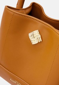 Brown leather tote bag with a textured gold woven accent on the front, featuring a smooth finish and structured shape.