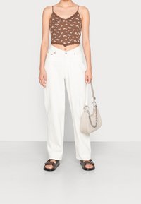 Top corto de flores marrón con encaje en los bordes, combinado con pantalones de pierna ancha blancos de tiro alto y sandalias negras con tiras; sosteniendo un bolso gris claro.