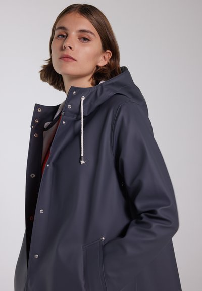 Marine vandtæt regnfrakke med hætte, sølvfarvede trykknapper og snoretræk ved halsen. Har en glat tekstur og frontlommer.