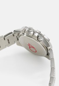 Montre chronographe en acier inoxydable avec un bracelet argenté, trois poussoirs et une lunette texturée comportant un logo rouge au dos du boîtier.