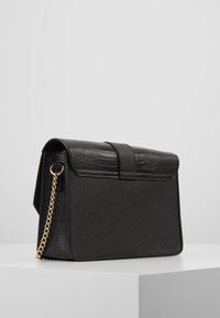 Czarna torebka z teksturowanym wykończeniem, z klapą i złotym łańcuszkiem. Ma wyraźnie zarysowany prostokątny kształt.