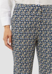Geweven broek in blauw, crème en zwart; geometrisch ontwerp met vormen in rijen. Kenmerkt zich door een gladde stof en een tailleband. Hand zichtbaar.