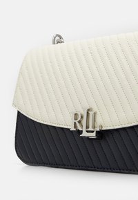 Vadderad läderhandväska med en krämfärgad övre klaff och marinblå kropp, med en logo i silverfärg och diskret magnetstängning.