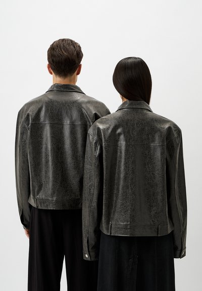 Zwei Personen tragen schwarze Kunstlederjacken mit strukturiertem Finish, die einen klassischen Kragen und sichtbare Nähte auf dem Rücken haben.