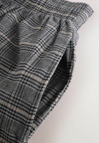 Szara tkanina w kratę z naprzemiennymi czarnymi i beżowymi liniami, posiadająca elastyczny pas i marszczoną teksturę u góry.