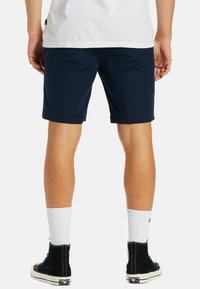 Navy blue shorts made of lightweight fabric, featuring a straight cut, side pockets, and a clean finish. Worn with black shoes and white socks.