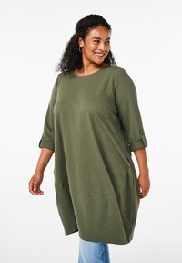 Olivgrön översize tunika med 3/4 ärmar, rundad halsringning och sidfickor, tillverkad av mjukt tyg med slät yta.