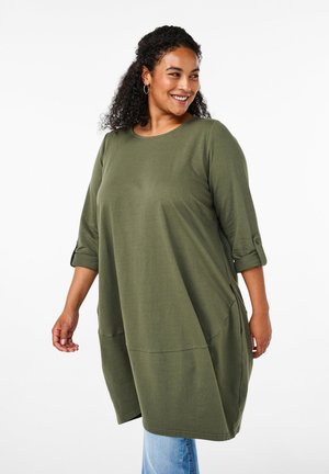 Tunique oversize vert olive avec des manches 3/4, un col rond et des poches latérales, fabriquée dans un tissu doux avec une texture lisse.