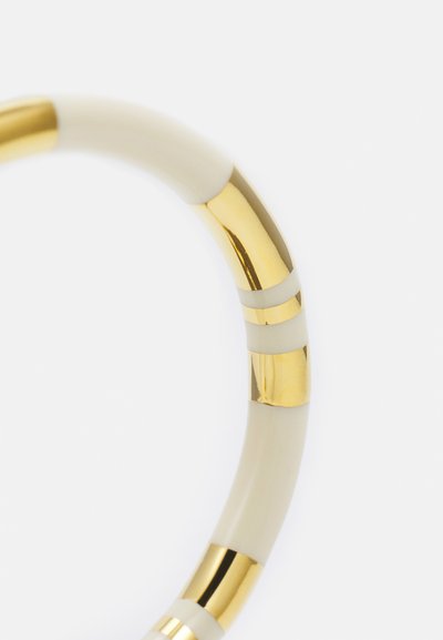 Gold-accented bangle with alternating sections of smooth cream and glossy gold-tone metal, showcasing a curved, tubular design.