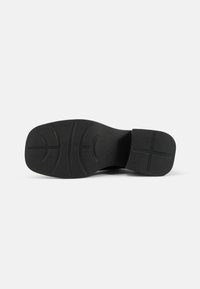 Black shoe sole with a textured rubber surface; features a patterned grip and a slight heel. Symmetrical design with curved lines.