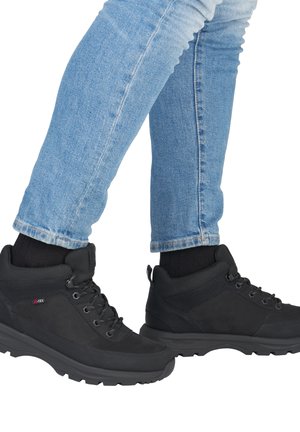 Schwarze Wanderschuhe mit strukturiertem Stoff, Schnürung und gepolstertem Schaft. Tragen Sie dazu eine blaue Jeans mit Umschlag. Gummisohle für Trittfestigkeit.