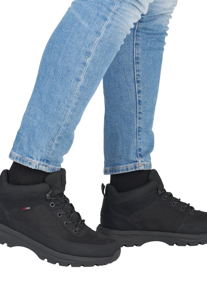 Zwarte wandelschoenen met textiel, veters en een gevoerde kraag. Draagt een blauwe denimjeans met een omslag. Rubberen zool voor grip.