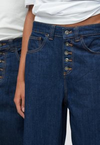 Τζιν παντελόνια σε σκούρο μπλε με σχεδίαση ψηλής μέσης, με πέντε κουμπιά, πορτοκαλί ραφές και μπροστινές τσέπες. Ύφασμα μείγματος βαμβακιού.