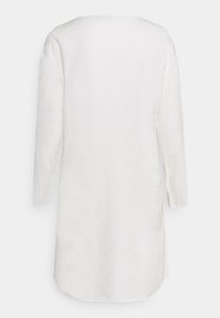 Robe blanche en coton à manches longues, coupe droite et ourlet arrondi, vue de dos sur un fond uni.