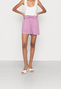 Ljuslila shorts med elastisk midja och dragsko. Matchas med en vit, ärmlös topp och öppna vita mules.