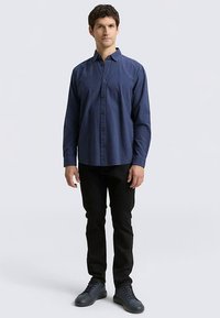 Marineblauw geruit overhemd met knopen, lange mouwen, een kraag en een borstzak, gecombineerd met zwarte broek en grijs schoeisel.