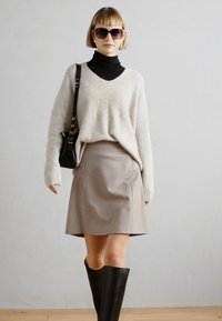 Jasnoszary sweter dzianinowy na czarnym golfie, zestawiony z beżową spódnicą w kształcie litery A i czarnymi kozaczkami do kolan. Dodatki obejmują duże okulary przeciwsłoneczne.