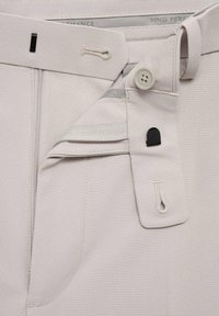 Pantalones beige con cierre de cremallera y botón, costuras decorativas y una cinturilla interna con acentos elásticos. Diseño ordenado y funcional.