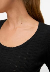 Top nero lavorato a maglia con scollatura a zigzag, caratterizzato da un motivo testurizzato con strisce verticali e piccoli disegni ad occhiello.