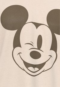 Beige puuvillapaita, jossa on suuri, sarjakuvamainen Mikki Hiiri -kasvo tummanharmaana, pyöreät korvat, winkkaava silmä ja leveä hymy.