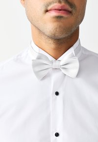 White dress shirt with a white textured bow tie and a thin matching collar band; features black buttons at the neck and chest.
