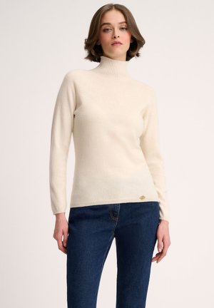 Cremefarvet turtleneck sweater lavet af blødt stof, med ribbede manchetter og kant, samt et lille guldlogo-akkord nederst til venstre.