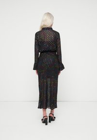 Μαύρο διάφανο φόρεμα με πολύχρωμες πουά, μακριά μανίκια και ζωνάκι στη μέση. Διαθέτει φαρδύ στρίφωμα και συνδυάζεται με μαύρες ψηλοτάκουνες σαγιονάρες.