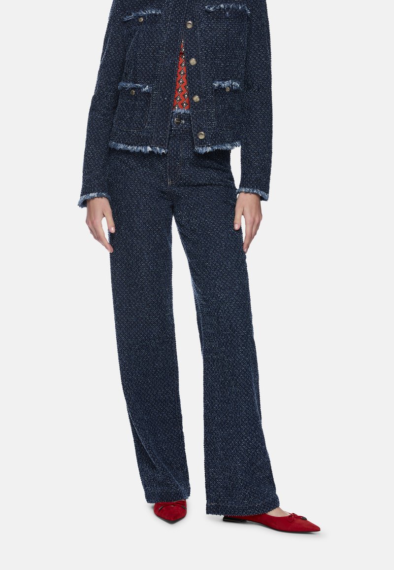 Marineblaue Tweedjacke mit Fransen, kombiniert mit passenden Wide-Leg-Hosen; ergänzt durch rote spitze Ballerinas und ein gemustertes Oberteil.