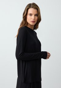 Zwart langslavend shirt van zacht stof. Heeft een ronde hals en slim fit mouwen, met een losse pasvorm bij de taille. Gladde textuur.
