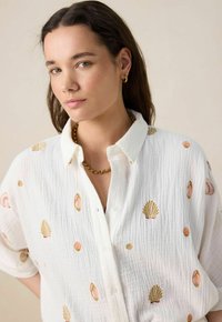 White button-up shirt with short sleeves, featuring gold and pink shell embroidery, textured fabric, and a relaxed fit.