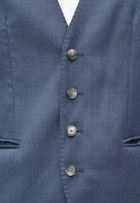 Ναυτικό μπλε γιλέκο με πέντε γκρι κουμπιά, διαθέτει γιακά σε σχήμα V, δύο πλαϊνές τσέπες και λεία υφασμάτινη υφή.