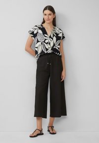 Blouse à manches courtes noir et blanc à motif floral associée à un pantacourt noir ample et des sandales noires. Textures lisses tout au long.