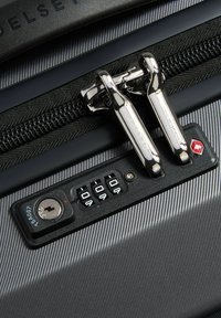 Combination lock and zipper pulls secured on a textured gray hard-shell suitcase with a TSA keyhole and a red diamond security logo.