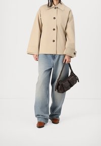 Beige skjortejakke, løstsiddende blå jeans, brune lædersko og en mørk læderhåndtaske med lommer, stående på en hvid baggrund.