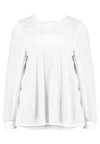 Blusa bianca a maniche lunghe con corpo testurizzato, dettagli in pizzo sulle spalle e sul petto, e una vestibilità rilassata. Tessuto liscio con polsini elastici.