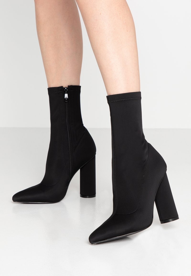 Les bottines en tissu noir présentent un bout pointu et une finition texturée. Elles comportent une fermeture éclair latérale et un talon haut carré.