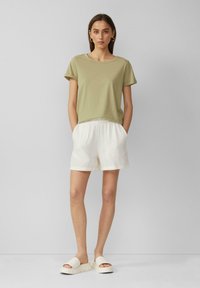 Olijfgroen T-shirt met korte mouwen, gecombineerd met witte gestructureerde shorts en chunky witte sandalen. Eenvoudige silhouet, casual ontwerp.