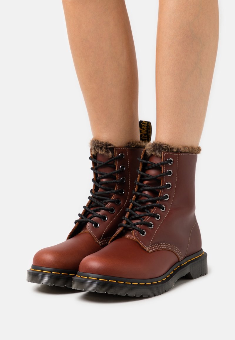 Bottes courtes en cuir marron avec col en fourrure, lacets noirs, coutures jaunes et semelle en caoutchouc texturée. Conçues pour la durabilité et le confort.