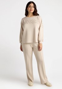 Beige sweatshirt with decorative studs across the chest, paired with matching beige trousers, both in a soft fabric blend with relaxed fit.
