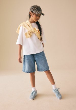 Balti trumpomis rankovėmis marškiniai, šviesiai mėlyni džinsiniai šortai, geltonas megztinis uždėtas ant pečių ir kepurė su leopardų raštu. Šviesiai mėlyni sportbačiai su baltais padais.