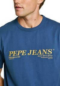 Mėlynas medvilninis marškinėlis su apvalia iškirpte, su geltonu "PEPE JEANS" logotipu ir tekstu. Paprastas dizainas, be papildomų raštų ar akcentų.