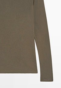 Olive green long-sleeve top made of ribbed fabric. Features a straight cut with side slits and finished hems.