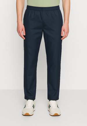 Pantaloni con vita elastica di colore blu navy con design a gamba dritta. Il tessuto appare liscio e senza fantasie, abbinato a sneakers di colore chiaro.
