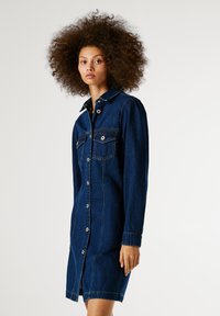 Tumši zila džinsu kleita ar pogu aizdari priekšā, divām krūšu kabatām, garām piedurknēm un apkakli. Iezīmē kontrastējoša šuvēšana un pieguļošs siluets.