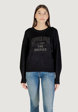 Maglione nero con collo rotondo, vestibilità ampia e maniche lunghe. Presenta la scritta "GUESS EST 1981 LOS ANGELES" in lettering metallico e decorazioni.