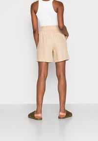 Beżowe lniane szorty z szerszym elastycznym pasem, gładką fakturą i bocznymi kieszeniami, w połączeniu z brązowymi sandałami wsuwanymi.